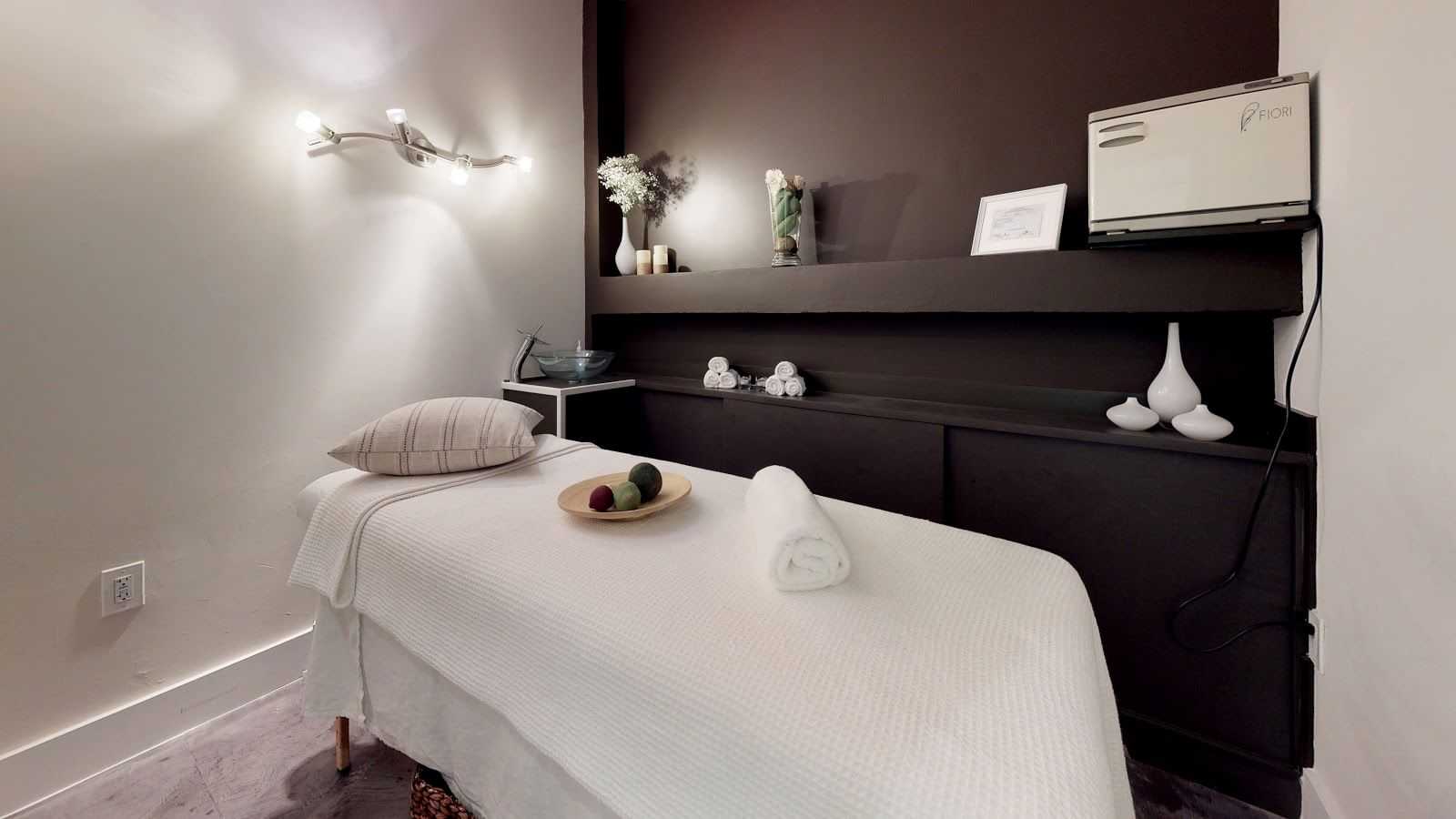 Massage room with a neatly prepared bed, cozy lighting, and relaxing decor.