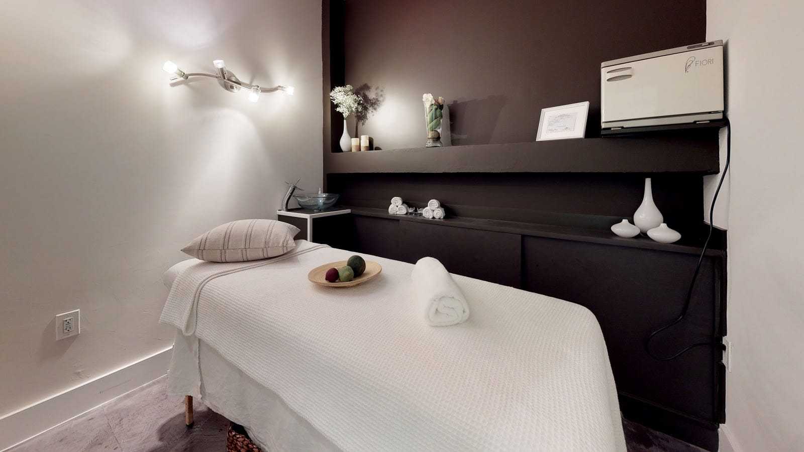 Massage room with a neatly prepared bed, cozy lighting, and relaxing decor.