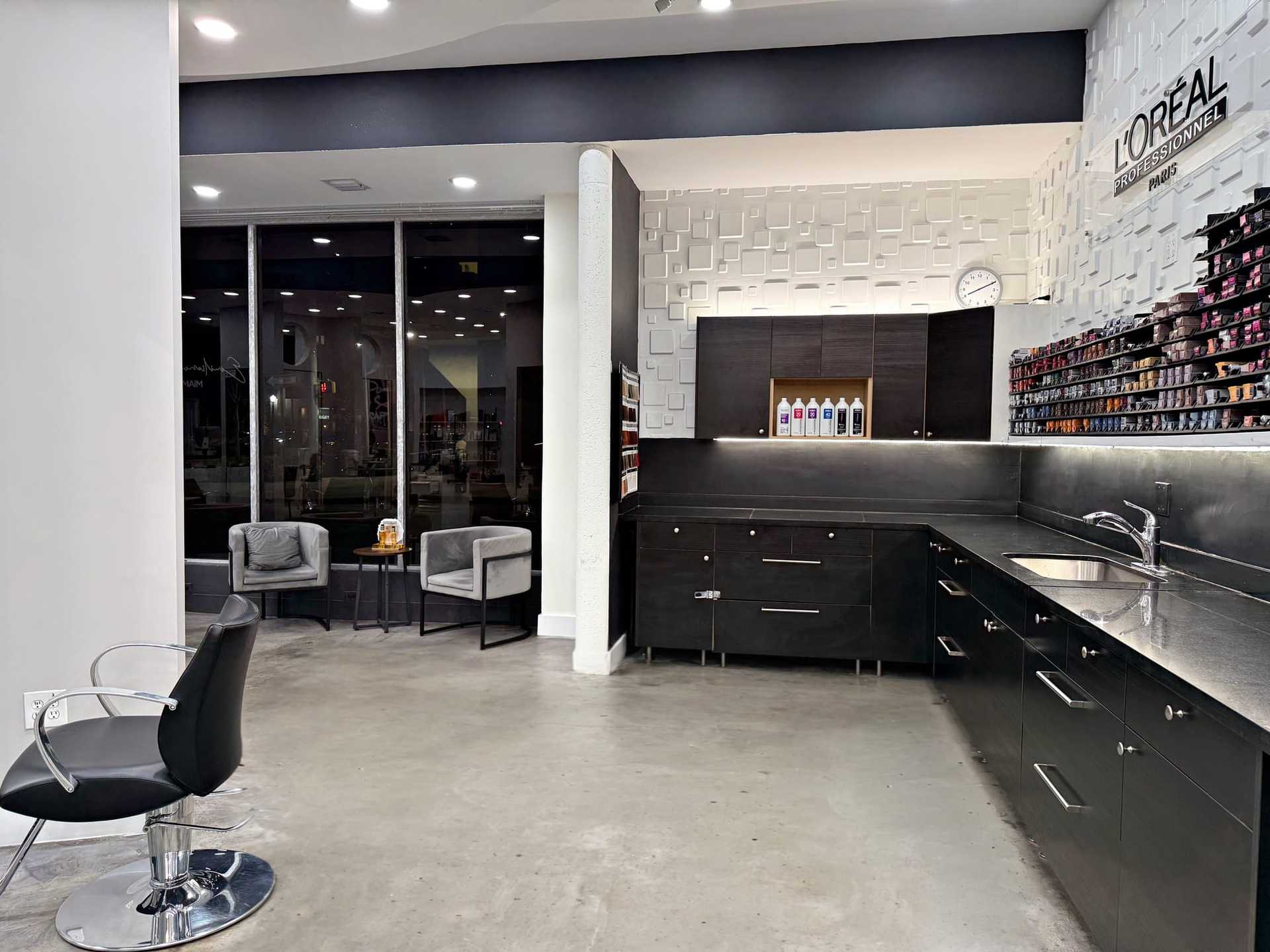 Modern hair salon with styling stations, chairs, product shelves, and sleek black cabinets.